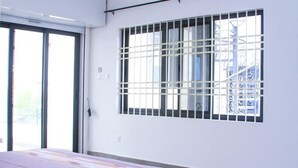 Une pièce avec un lit, une fenêtre avec des barreaux et une porte donnant sur l’extérieur.