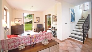 Un salon spacieux avec un canapé, une table basse et un téléviseur. Un escalier avec une rampe mène à l’étage supérieur.