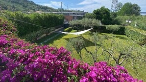 Un jardin avec un hamac, une haute structure métallique et un bâtiment en arrière-plan.
