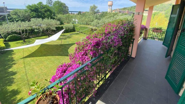 Un balcon donnant sur un jardin bien entretenu, un château d’eau et une haute structure visible au loin.