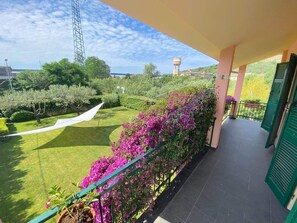 Un balcó amb vista a un jardí ben cuidat, un aiguabarreig i una construcció alta a la distància.
