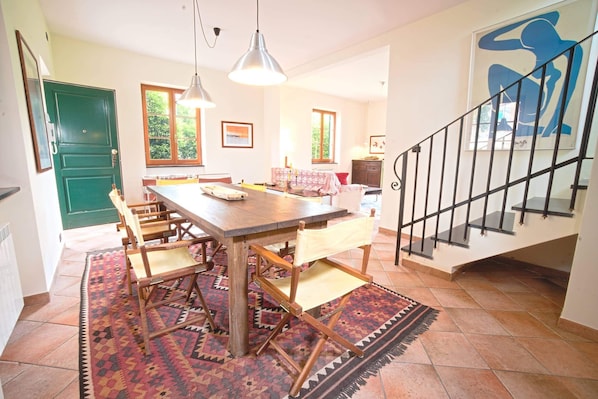 A dining area with a wooden table and chairs, a patterned rug, and a staircase with a railing.