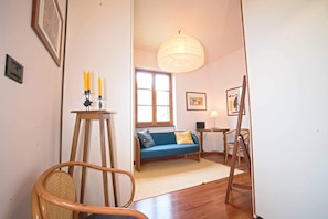 A room with a wooden floor, a blue sofa, a standing lamp, and a framed picture on the wall.