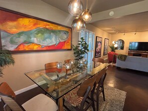 A dining area with a glass table, chairs, and a painting of a fish.