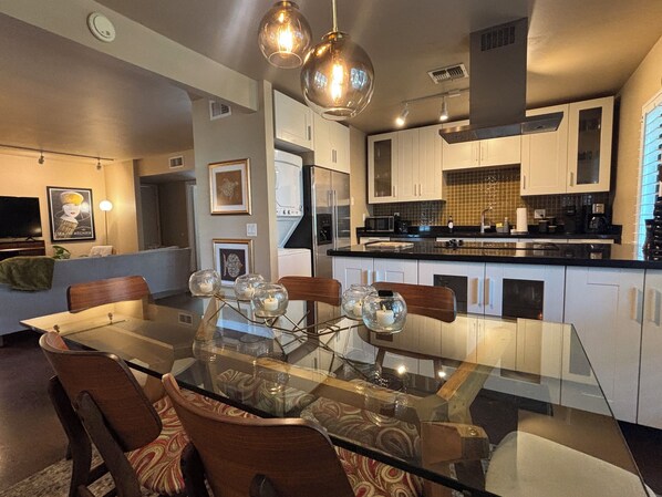 A modern kitchen with white cabinets, a black countertop, and a glass dining table with chairs.