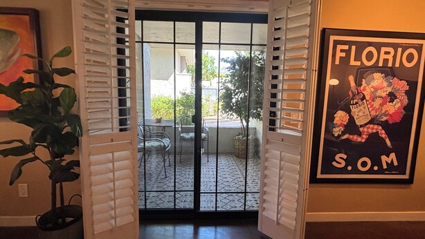 A doorway leading to a patio area with a table and chairs, a potted plant, and a framed poster on the wall. - Well Appointed fully furnished 2BR, 2Bath, 1st floor, Guard-Gated, Biltmore area (Phoenix)