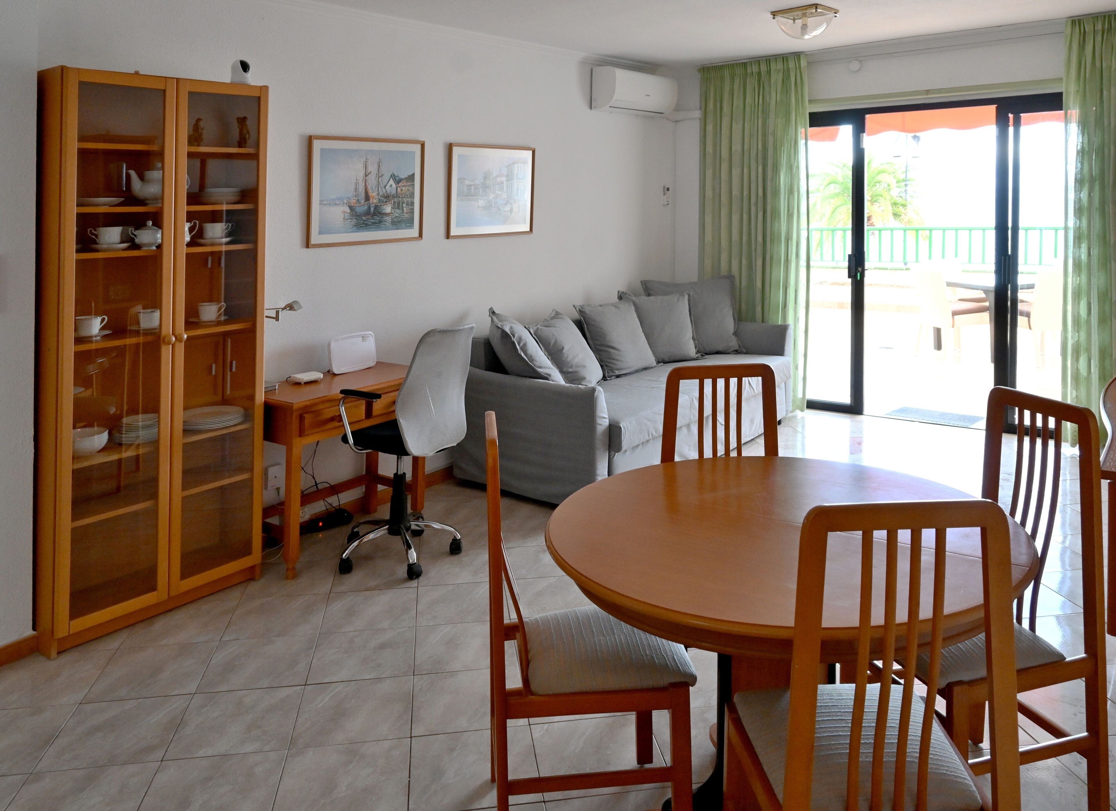 A living room with a dining area, a sofa set, a wooden cabinet with dishes, and two framed pictures on the wall.
