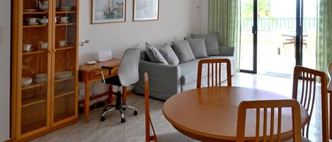 A living room with a dining area, a sofa set, a wooden cabinet with dishes, and two framed pictures on the wall.