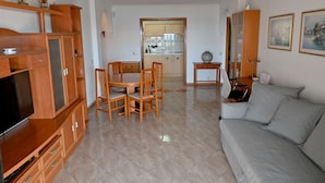 A living room with a sofa, TV, wooden cabinets, and a dining area with chairs and a table. - 1st Line Sea View · Plaza Terrace (Santiago del Teide)