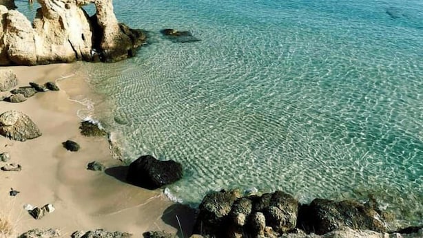 Un paysage côtier caractérisé par une eau turquoise cristalline, des formations rocheuses et une plage de sable.