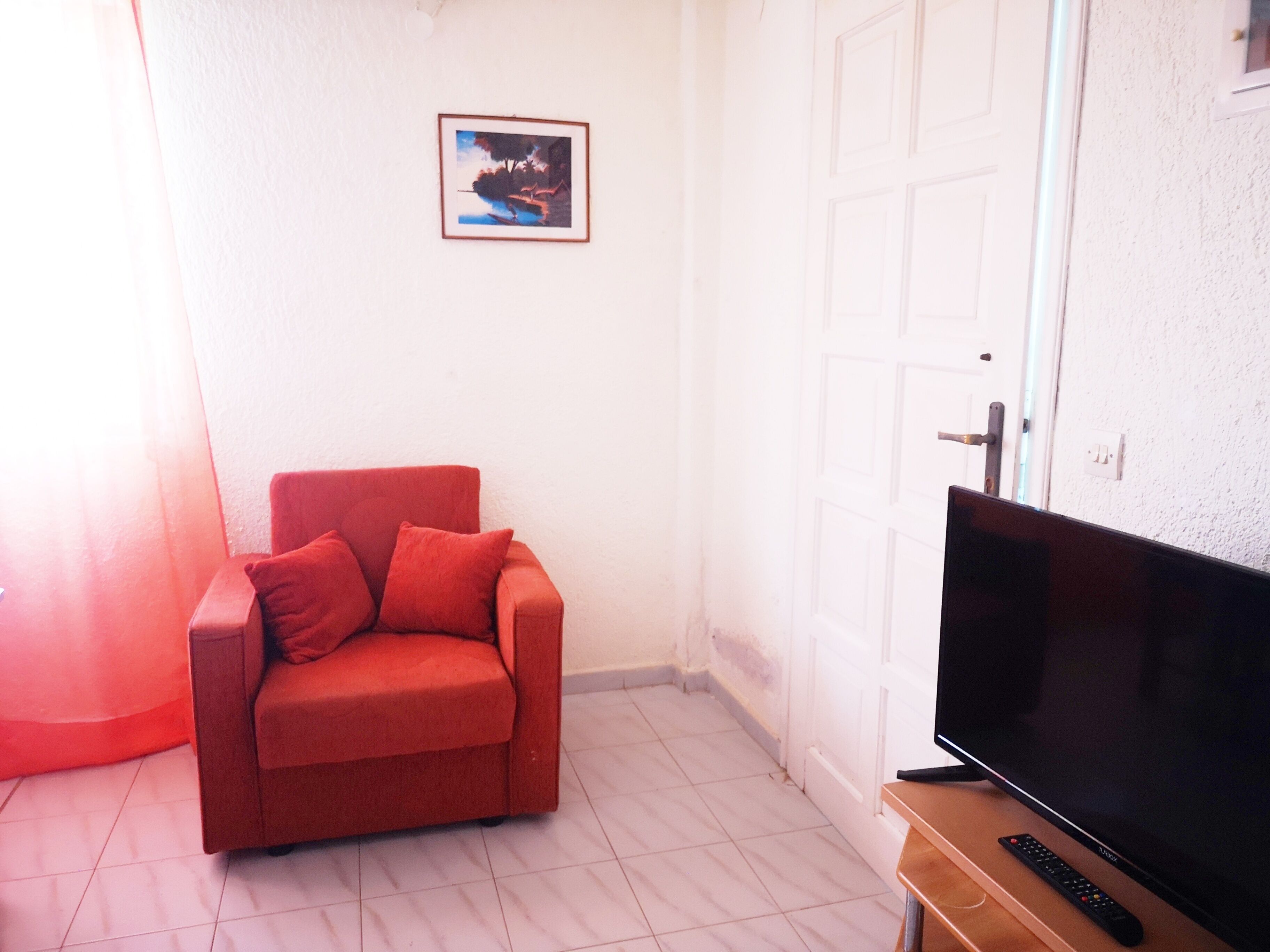 A room with a red sofa, a television on a wooden stand, and a door with a white frame.