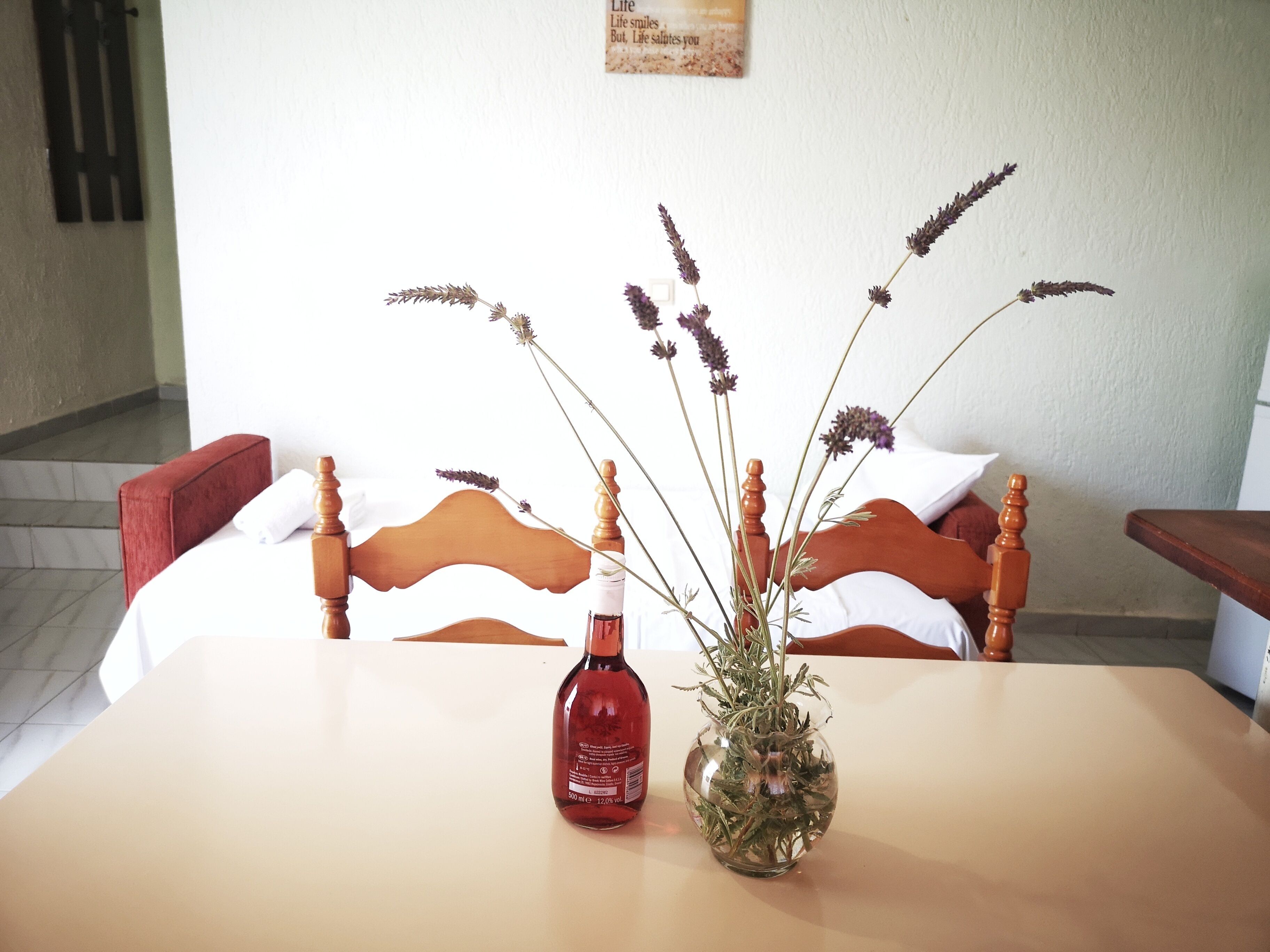 Una habitación de hotel con una cama de madera, una mesa con una botella y un jarrón de flores secas.