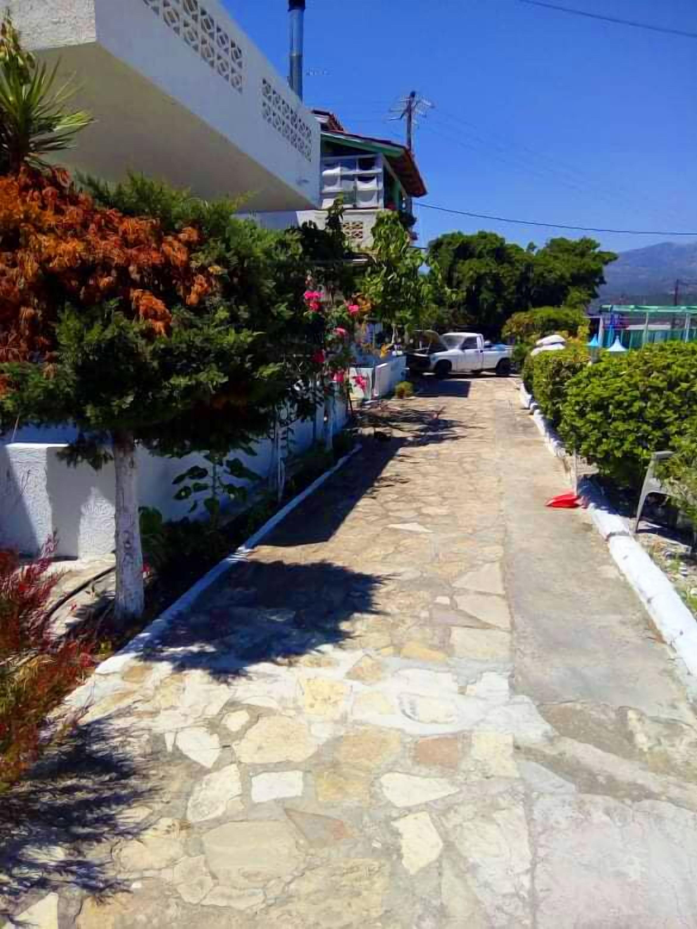 A stone-paved pathway leading to a building with a white facade and a balcony.