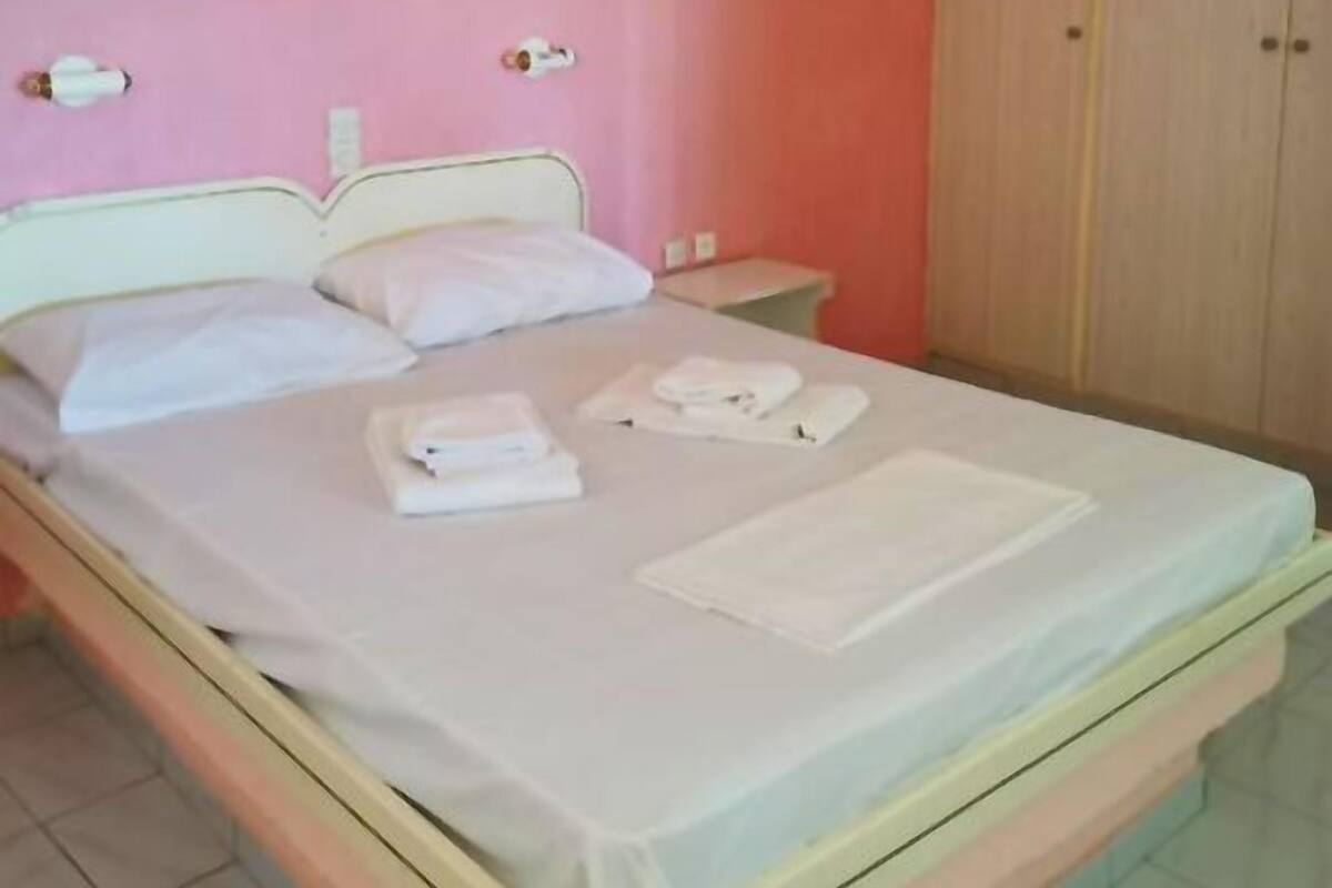 A single bed with white linens, a nightstand, and a wardrobe in a room with pink walls.