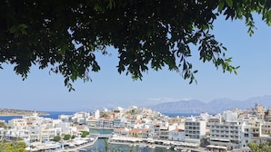 Un paysage urbain côtier avec des bâtiments le long d’une promenade, un port de plaisance et des montagnes en arrière-plan.