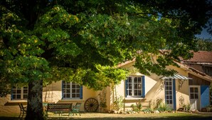 Ein Haus mit einem großen Baum davor, einer Bank und einem Wagenrad.