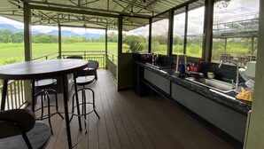 Ein überdachter Außenbereich mit Tisch und Stühlen, einer Küchenzeile und Blick auf eine grüne Landschaft.