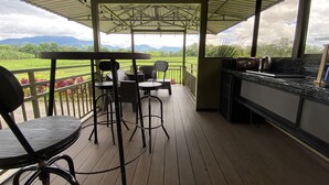 Ein überdachter Außenbereich mit Holzdeck, einer Bar mit Spüle sowie Stühle und Tische zum Essen.