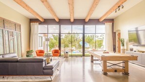 Amplia sala de estar con mesa de billar, asientos cómodos y grandes ventanales con vistas al exterior.