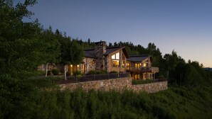 A large stone house with multiple balconies and large windows, surrounded by lush greenery. - Outpost: Teton Retreat - Expansive Teton Views (Jackson)