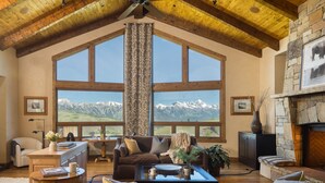 A spacious living room with a large window offering a mountain view, a stone fireplace, and a cozy seating area. - Outpost: Teton Retreat - Expansive Teton Views (Jackson)
