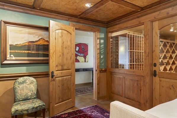 A wooden-paneled room with a door leading to a hallway, a framed landscape painting, a chair, and a patterned rug.