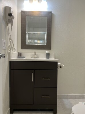 Een badkamer met een donkere wastafel, een spiegel boven de wastafel, en een toilet in de achtergrond.