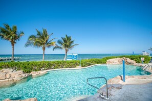 A clear blue pool with a view of the ocean and palm trees. - Castaways Cove Unit 122  Beach Front direct access (East End)