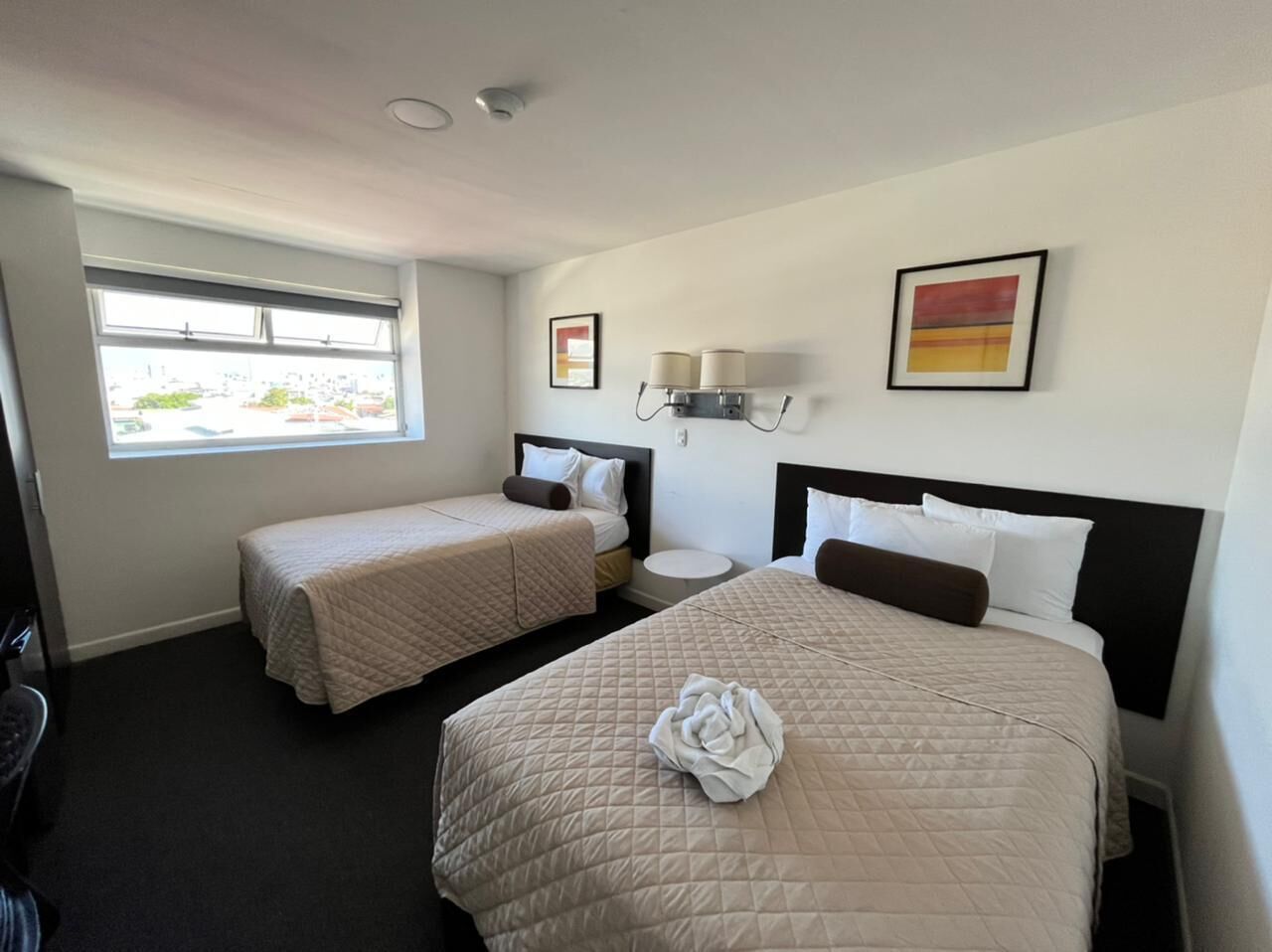 Una habitación de hotel con dos camas, una ventana, una lámpara de pared y un cuadro.