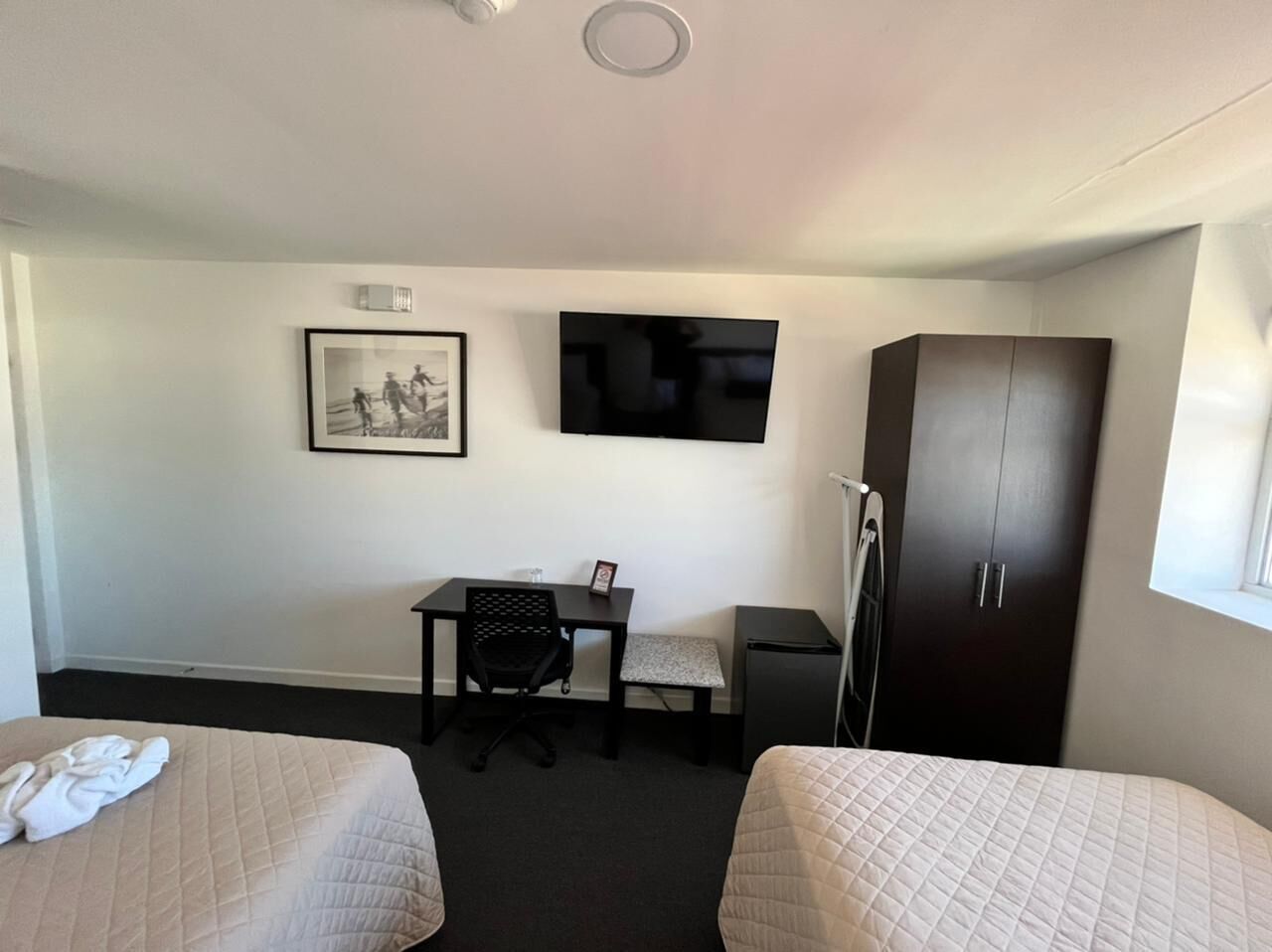 A hotel room with two beds, a desk with a chair, a television, and a wardrobe.