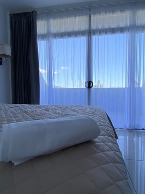 Une chambre d’hôtel avec un grand lit, une fenêtre ornée de rideaux légers et une vue sur le paysage urbain.