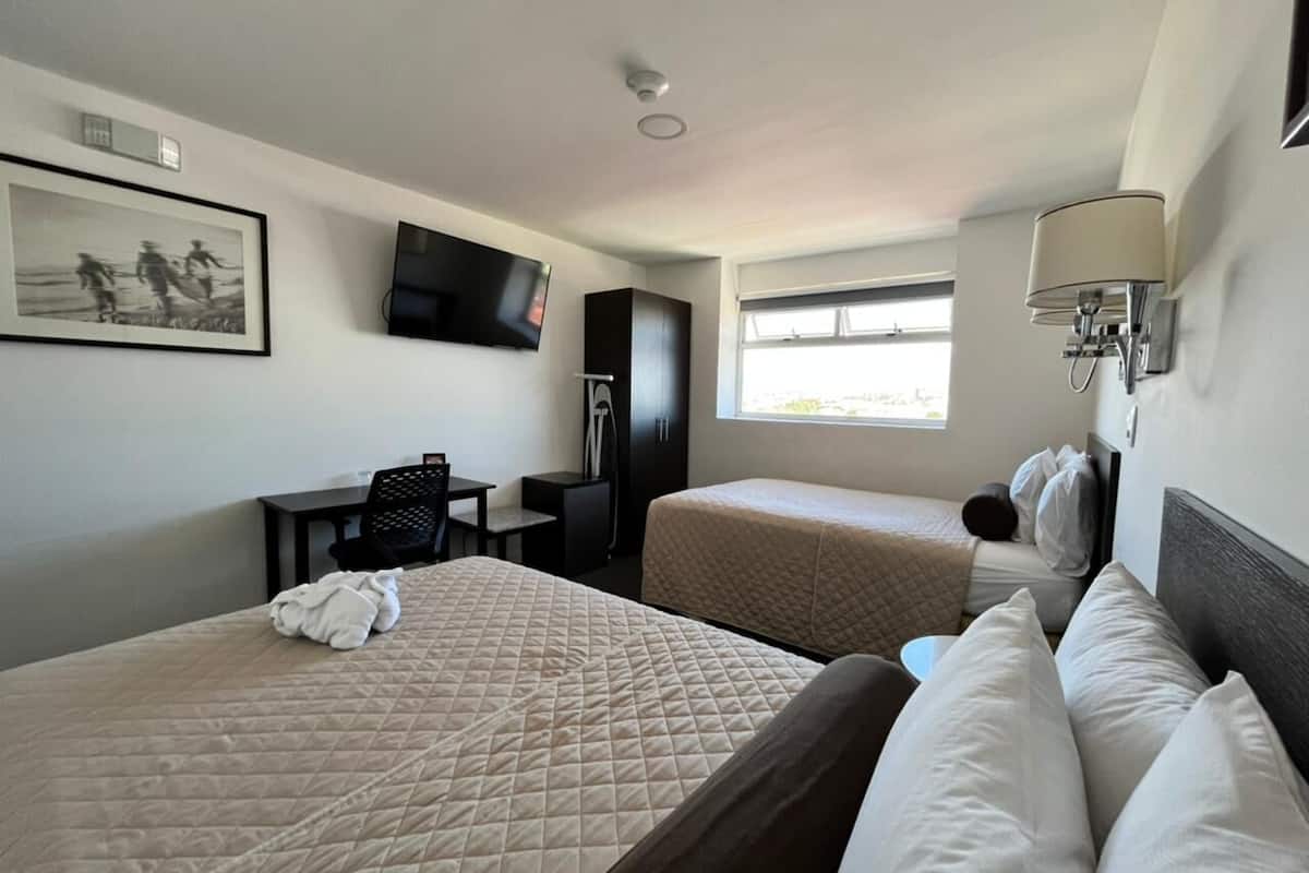 Een hotelkamer met twee bedden, een bureau, een televisie en een raam.