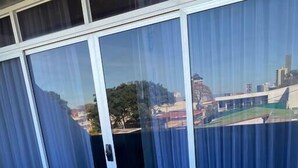 A balcony with a view of a cityscape, featuring a glass door with curtains, and a tiled floor. - Apartahotel Altos de la Sabana (San José)