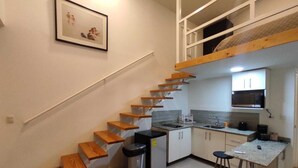 A compact kitchen with a built-in microwave, a sink, and a small dining area with stools. - Apartahotel Altos de la Sabana (San José)