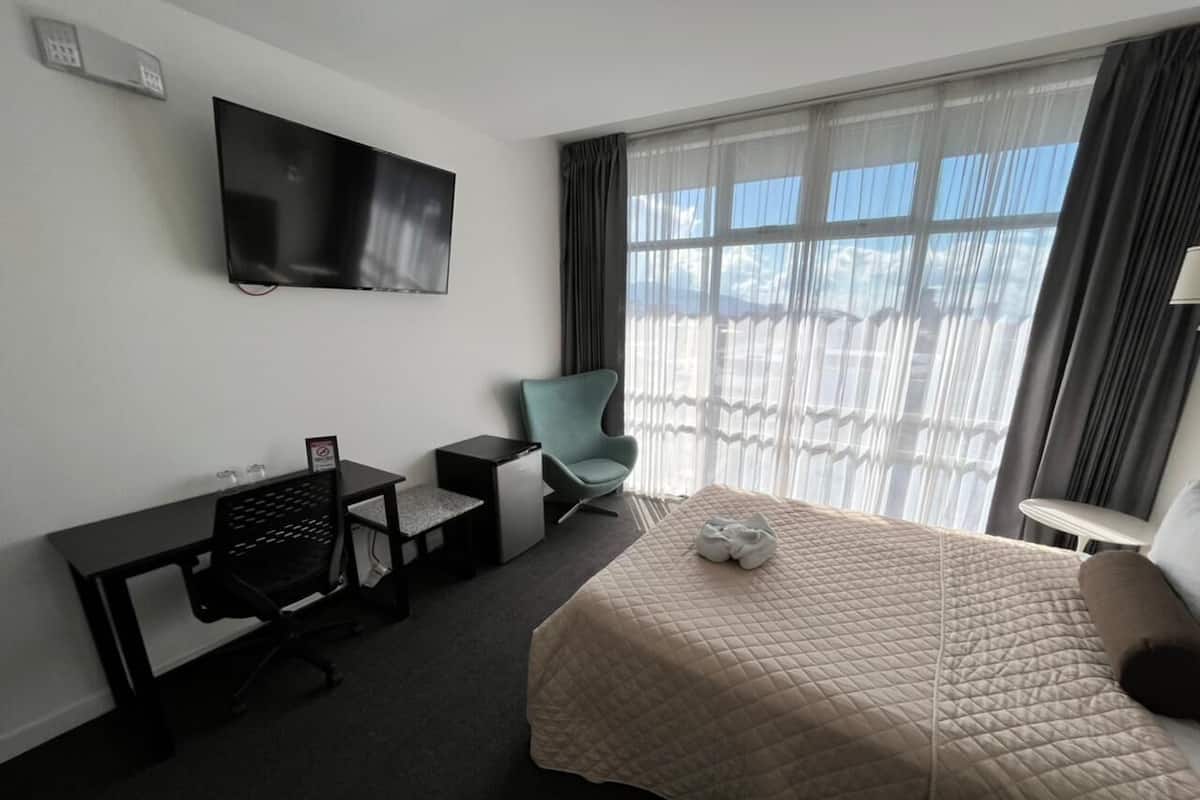 Een hotelkamer met een bed, een bureau, een stoel, een televisie en een raam met gordijnen.