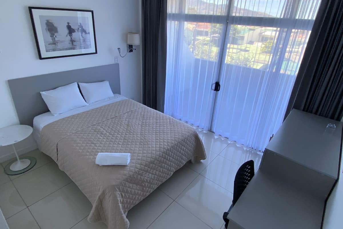 Een hotelkamer met een bed, bureau, stoel, lamp en raam met gordijnen.