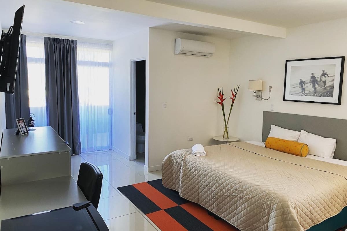 Een hotelkamer met een bed, bureau, stoel, televisie en een foto aan de muur.