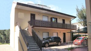 Un edificio de dos pisos con un balcón, una escalera y un coche estacionado.