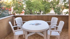 Una mesa redonda con cuatro sillas blancas en un patio con baldosas.