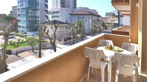 Varanda com cadeiras e mesa de plástico branco, com vista para um horizonte urbano com edifícios e árvores.