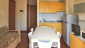 Uma cozinha compacta com armários amarelos, uma mesa de jantar branca e um sofá.