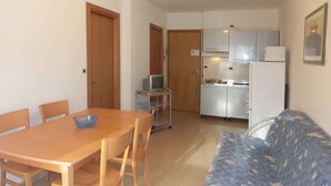 En kompakt opholdsstue med spisebord, stole, sofa, tekøkken og fjernsyn.