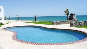 A swimming pool with a curved edge, surrounded by a stone wall and a paved walkway. - Paradise Villa 19 by Kivoya (Puerto Peñasco)