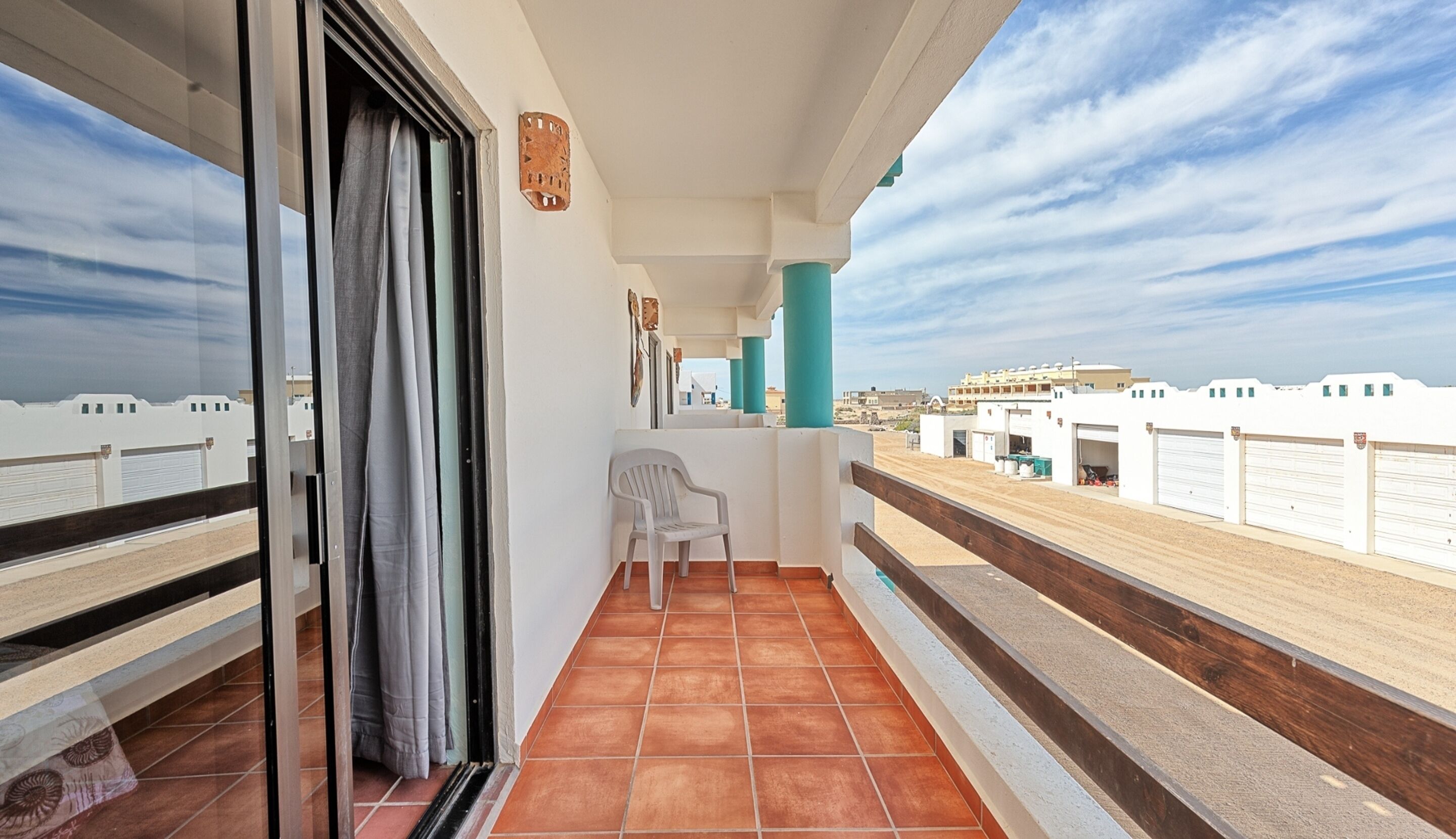 A balcony with a view of the cityscape, a chair, and a window with curtains.