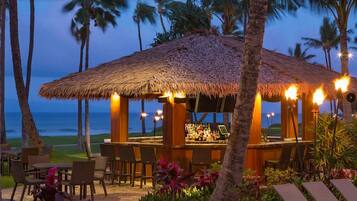 A thatched-roof bar area with outdoor seating and a view of the ocean.
