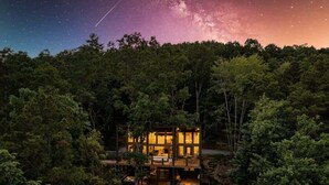 A modern, multi-level cabin nestled in a forest, with large windows allowing views of the night sky and a visible Milky Way. - Mountain Abode - Hot tub & mountain views (Blue Ridge Mountains)