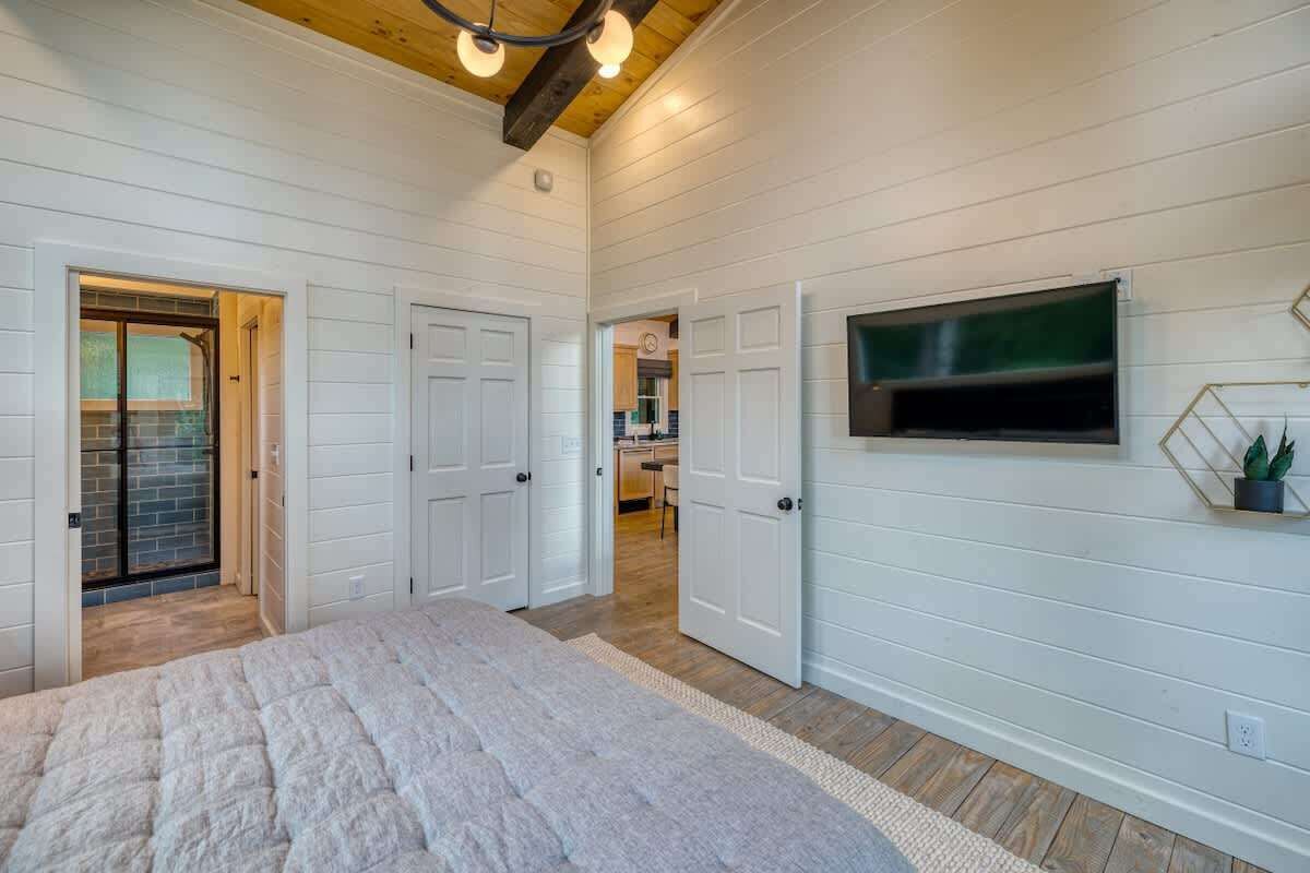 Une chambre avec un grand lit, des murs recouverts de panneaux blancs, un plafond en bois et un téléviseur fixé au mur.