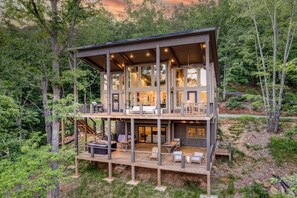 Une cabane en bois à plusieurs niveaux, dotée d’une terrasse et entourée de forêt.