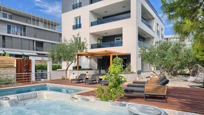 Een modern zwembadterras met ligbedden, een jacuzzi en een pergola.
