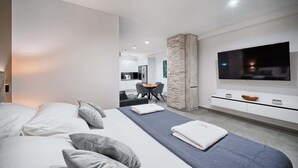 Een moderne slaapkamer met een groot bed, een televisie en een eethoek op de achtergrond.